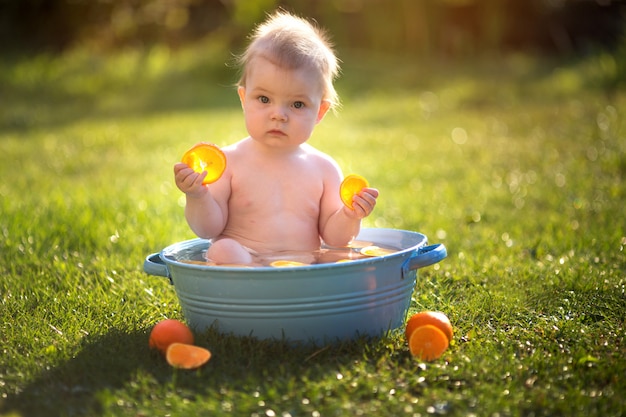 Niño pequeño se baña en el parque con naranjas