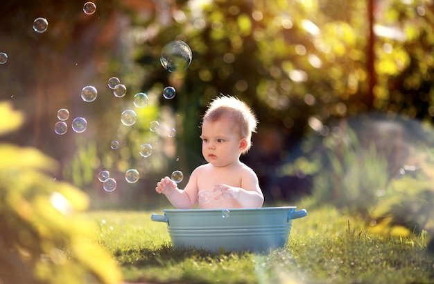 Niño pequeño se baña en el parque con pompas de jabón