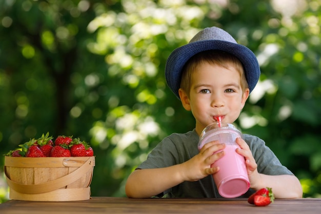 niño pequeño bebiendo batido de fresa de un vaso de plástico desechable al aire libre