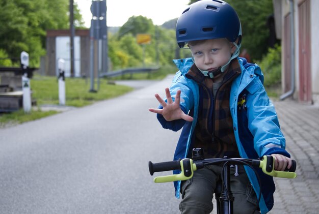 Un niño pequeño en una bicicleta extendió su palma delante con una llamada para detenerse