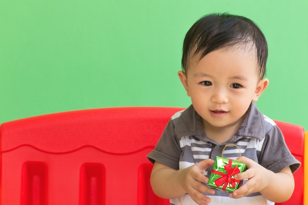 niño pequeño con caja de regalo en silla roja