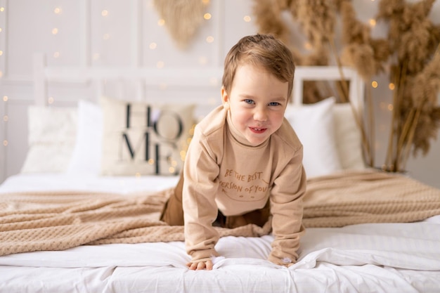 Un niño pequeño en una cama en tonos beige marrón natural se ríe y se regocija, un niño alegre y divertido está jugando en casa