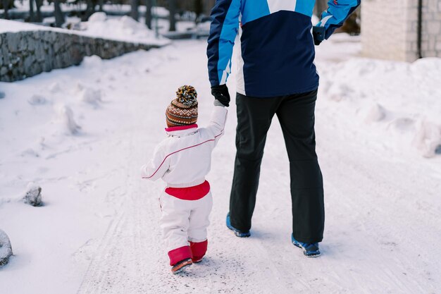 Niño pequeño camina por un camino nevado sosteniendo la mano de su padre Vista trasera recortada