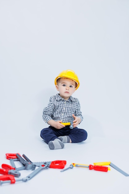 Un niño pequeño con una camisa a cuadros en la imagen de un constructor Un niño con un casco de construcción y herramientas de plástico