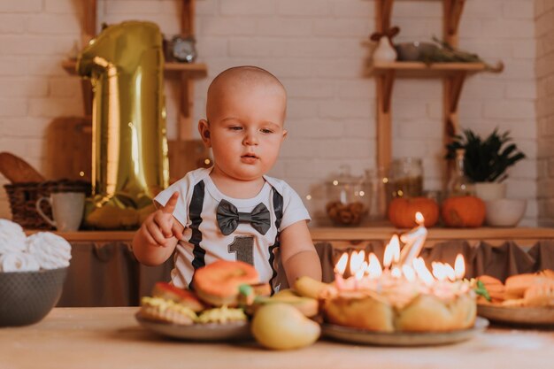 Un niño pequeño con una camiseta con el número uno extiende su mano hacia los dulces en la mesa. primer cumpleaños. dulces caseros saludables. malvaviscos, pan de jengibre, tarta de manzana, charlotte. foto de alta calidad