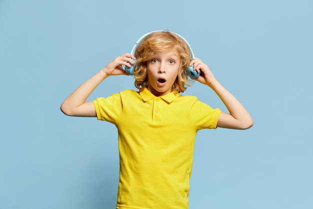 Niño pequeño con cara emotiva conmocionada posando en auriculares contra el fondo azul del estudio