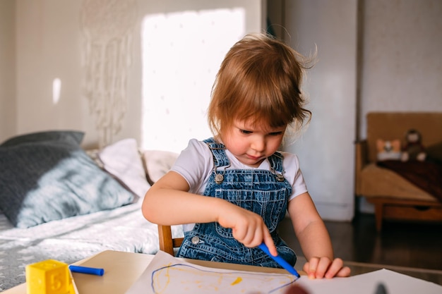 Niño pequeño en casa en la mesa de los niños dibuja con rotuladores