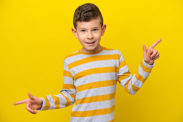 Niño pequeño caucásico aislado sobre fondo amarillo señalando con el dedo a los laterales y feliz