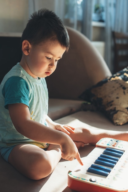 Niño pequeño caucásico está tratando de tocar el piano de juguete en el suelo