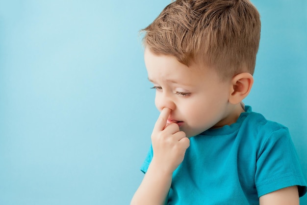 Niño pequeño caucásico hurgando su nariz sobre fondo azul