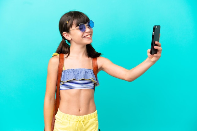 Niño pequeño caucásico yendo a la playa aislado de fondo azul haciendo un selfie