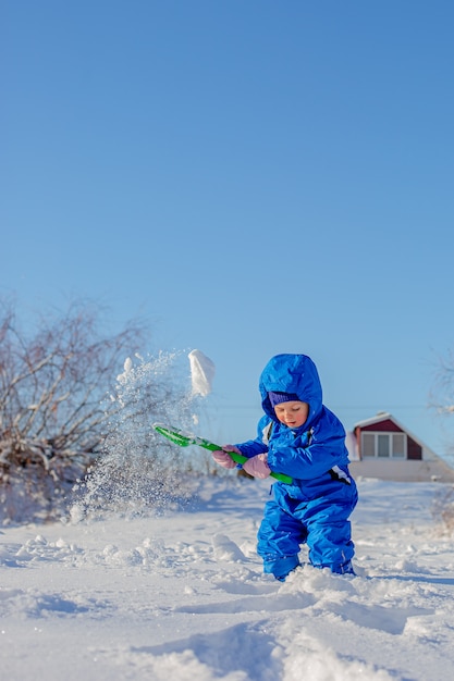 Niño pequeño cavar y jugar en la nieve del invierno, actividades de invierno para niños.