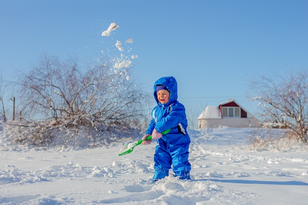 Niño pequeño cavar y jugar en la nieve del invierno, actividades de invierno para niños.