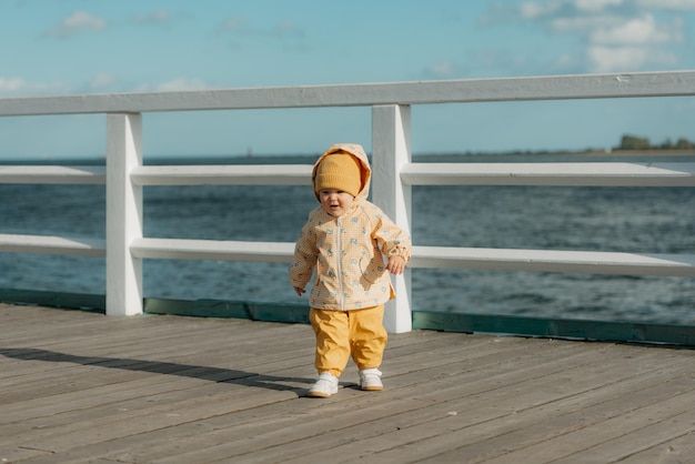 Un niño pequeño con una chaqueta amarilla y pantalones camina por el muelle