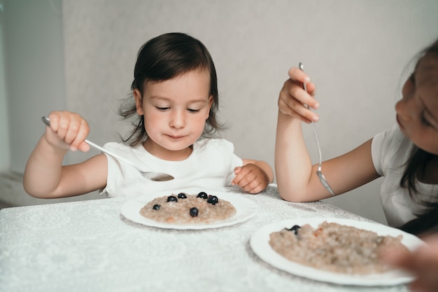 Un niño pequeño come avena con frutos rojos. La niña tiene una cuchara en sus manos