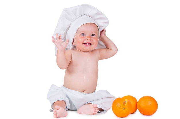 Un niño pequeño come una rodaja de naranja con un traje de chef sobre un fondo blanco.