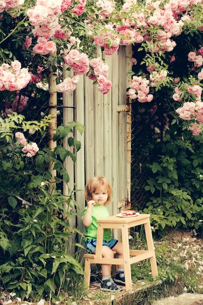 Niño pequeño comiendo cerca de rosal