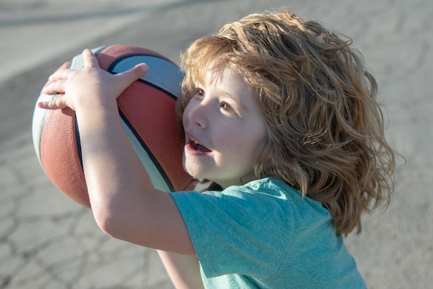 Niño pequeño de deportes caucásicos jugando baloncesto sosteniendo la pelota con cara feliz