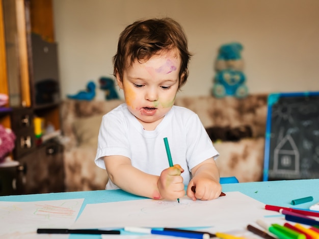 Un niño pequeño dibuja con rotuladores de colores en una hoja de papel.