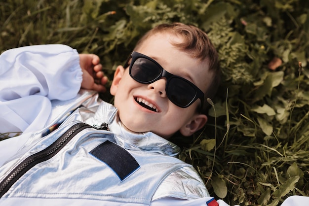 Foto un niño pequeño en un disfraz de astronauta está jugando afuera acostado en un campo en un día soleado