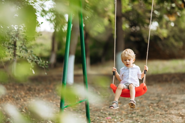 Niño pequeño divertido columpios en un columpio niño pequeño en un paseo en el parque de verano el concepto de niños