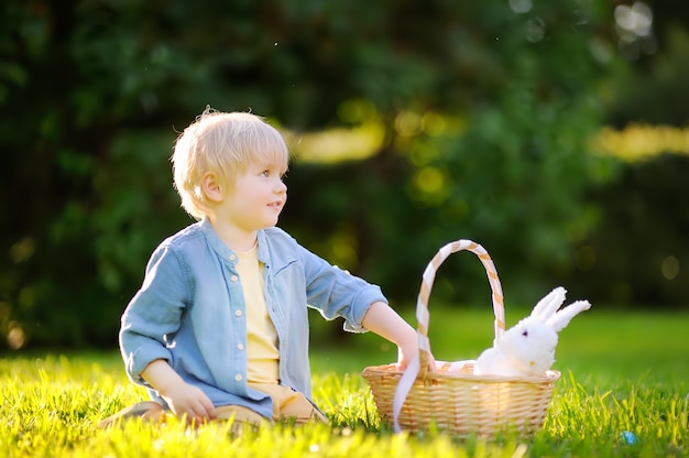 Niño pequeño encantador que caza huevos de Pascua en el parque de la primavera el día de Pascua