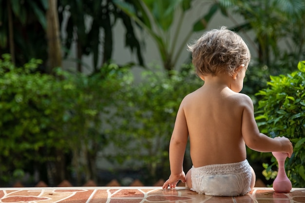 un niño pequeño encantador se sienta con un juguete en los escalones de una casa a la luz del sol. vista trasera.