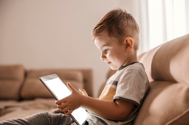 Un niño pequeño enfocado está usando una tableta con fines educativos mientras está sentado en una sala de estar