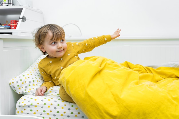 Niño pequeño está acostado en la cama. Niño que se despierta por la mañana.