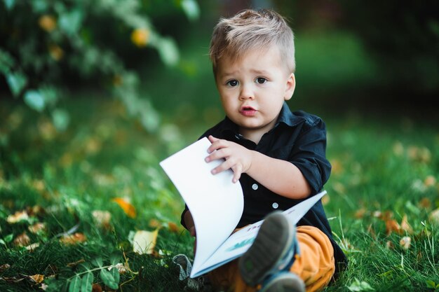 Un niño pequeño está leyendo un libro en el césped