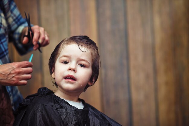 Un niño pequeño está recortado en las brillantes emociones del peluquero en su rostro.