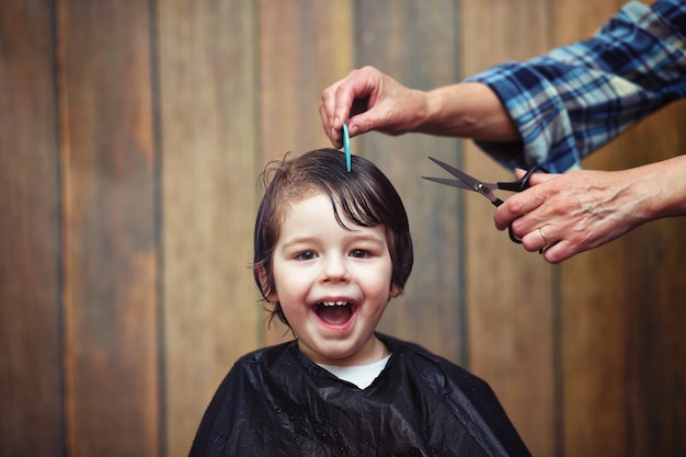 Un niño pequeño está recortado en las brillantes emociones del peluquero en su rostro.