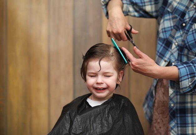 Un niño pequeño está recortado en las brillantes emociones del peluquero en su rostro.