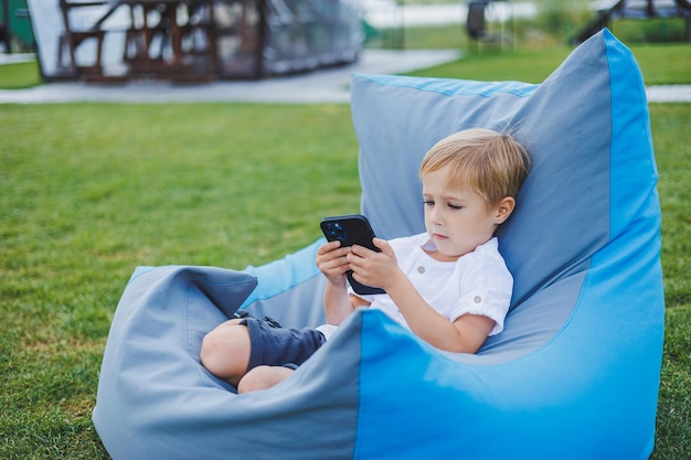 Un niño pequeño está sentado afuera en un día soleado y jugando juegos en el teléfono