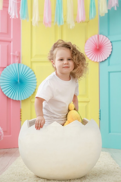 Un niño pequeño está sentado en un huevo blanco que eclosionó contra un fondo colorido de estudio