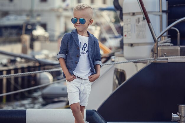 Un niño pequeño en un estilo marinero con el telón de fondo de barcos y yates.