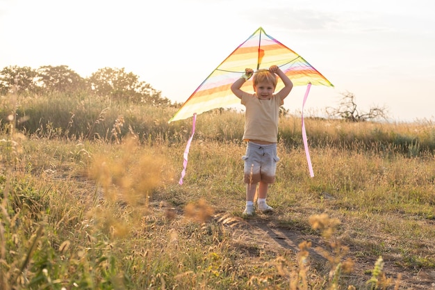 Niño pequeño feliz divirtiéndose con cometa en la naturaleza al atardecer