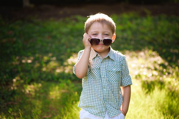 Niño pequeño feliz con las gafas de sol en el jardín.