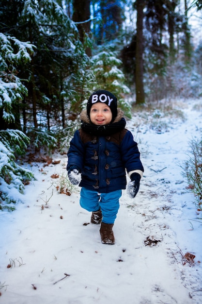 Niño pequeño feliz preguntándose los copos de nieve en el bosque de invierno