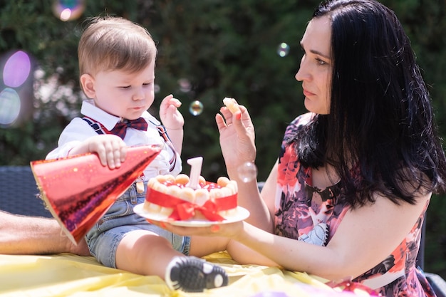 Un niño pequeño feliz con su madre celebra su cumpleaños con un sombrero de cumpleaños y un pastel y una vela