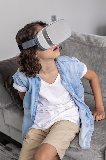 Niño pequeño feliz usando auriculares de realidad virtual gafas vr gesticulando en casa divirtiéndose