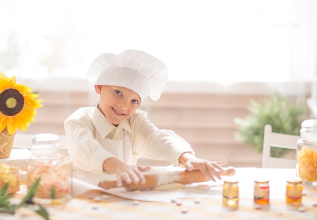 niño pequeño en forma de cocinero extiende la masa