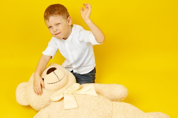 Un niño pequeño frustrado golpea a un oso de peluche con un fondo amarillo