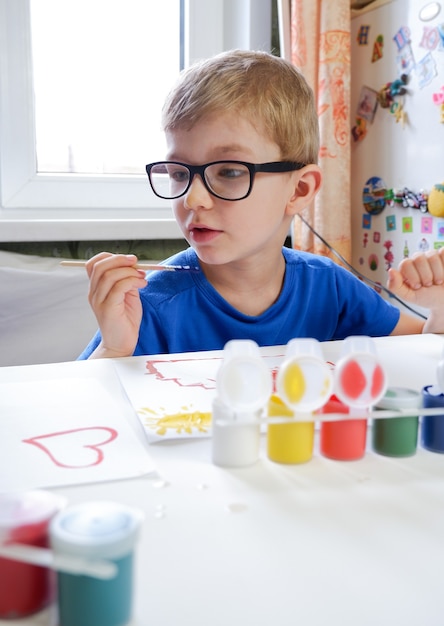 Un niño pequeño con gafas, dibujando con pintura. Creatividad infantil en casa.