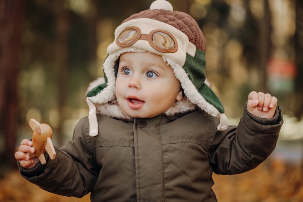 Niño pequeño en la gorra piloto jugando con avión de juguete en el parque. Otoño. Concepto