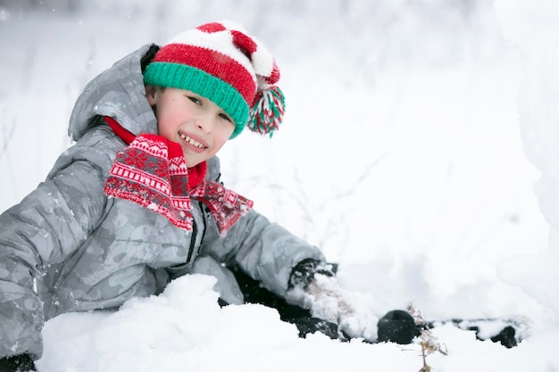 Un niño pequeño con un gorro de punto rojo juega en la nieve.