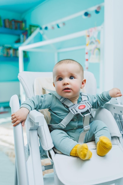 Un niño pequeño y guapo está sentado en una silla alta para alimentar a los niños Silla de cocina para comer Muebles para niños