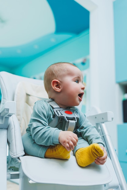 Un niño pequeño y guapo está sentado en una silla alta para alimentar a los niños Silla de cocina para comer Muebles para niños