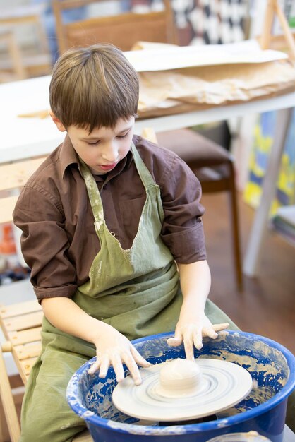 Un niño pequeño hace un producto de arcilla en un torno de alfarero.