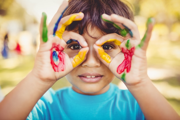 Foto niño pequeño haciendo gafas con sus manos pintadas